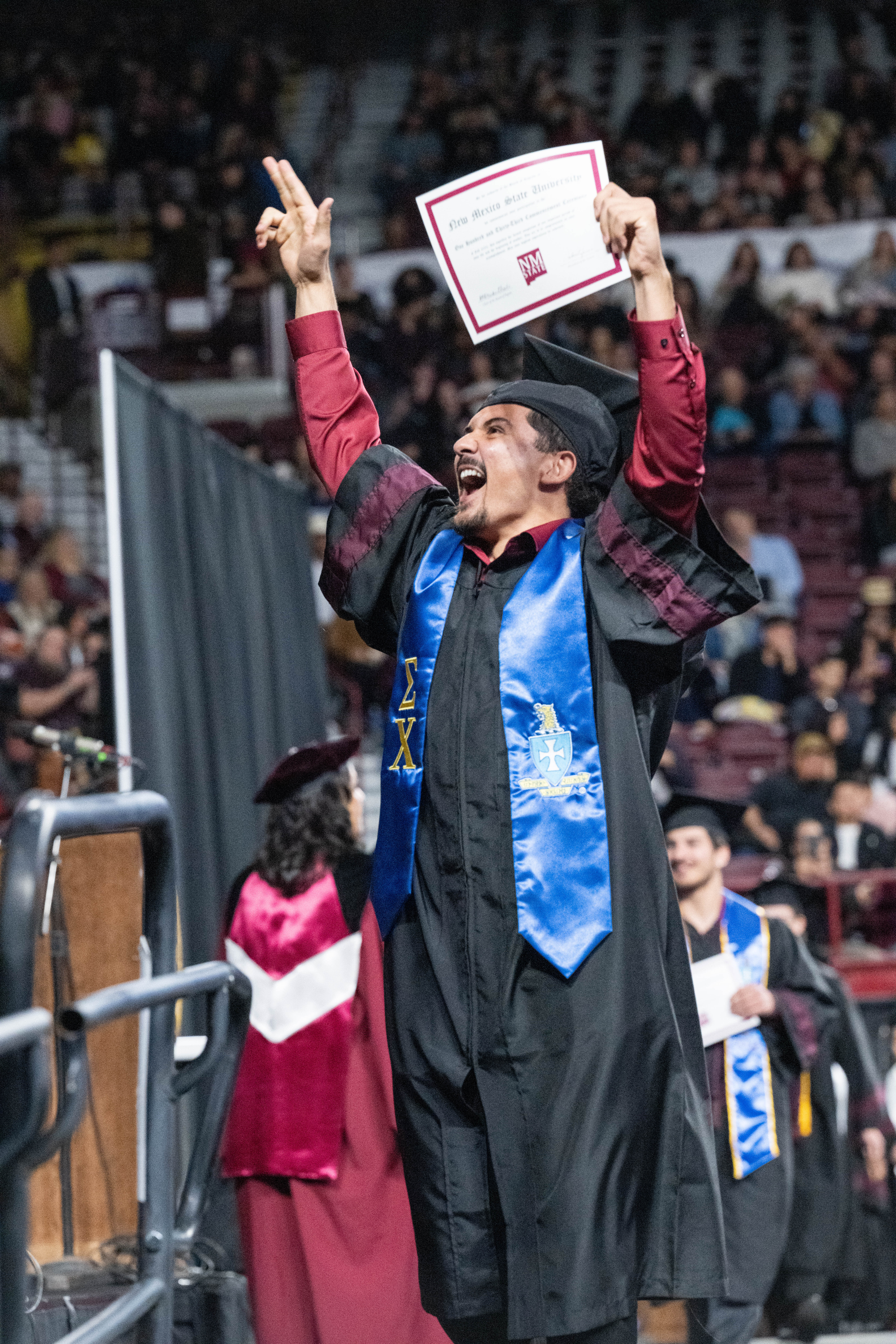 Graduate posing in front of NMSU gates