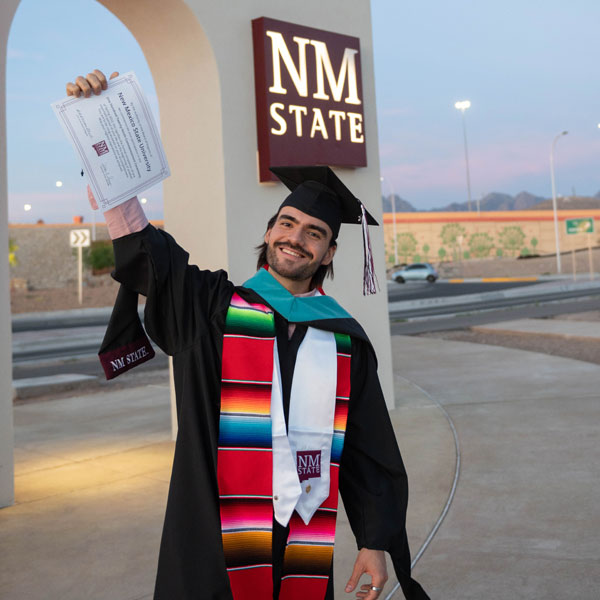 Graduate posing in front of NMSU gates